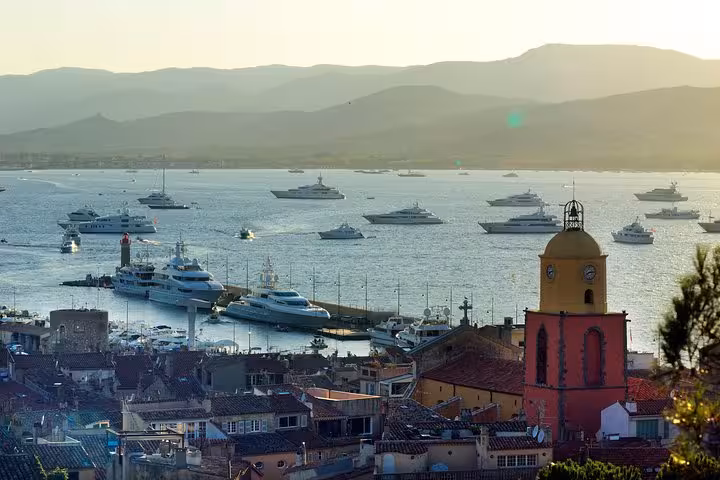 Aerial view of Saint-Tropez harbor with luxury yachts, colorful rooftops, and church bell tower at sunset