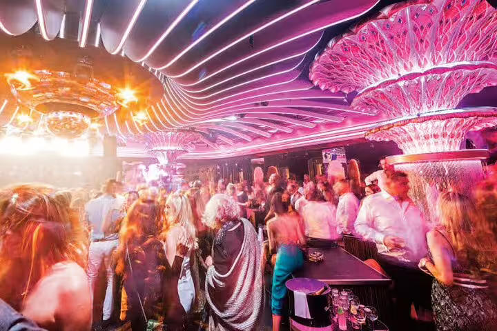 Crowded luxury nightclub in Saint-Tropez with pink neon lights and crystal chandeliers