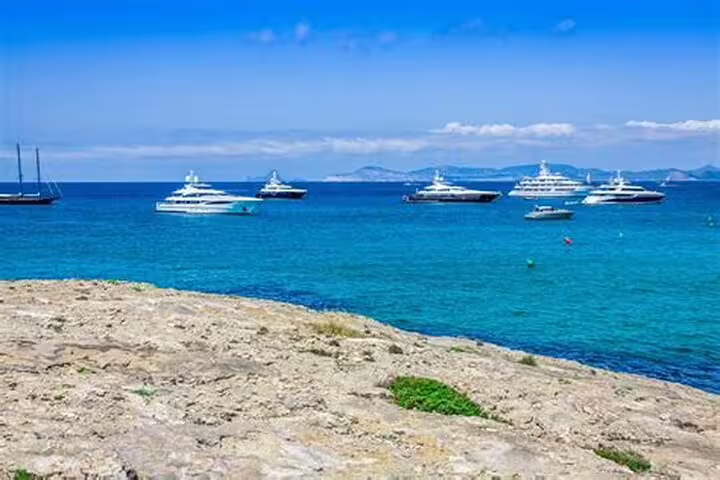 Luxury yachts anchored in turquoise waters near Saint-Tropez with rocky shoreline and mountains in background