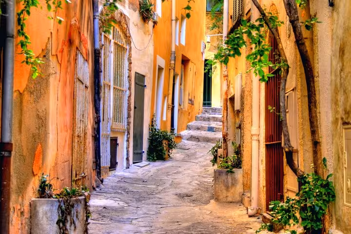 Narrow cobblestone alley with orange buildings and green plants in Saint-Tropez old town
