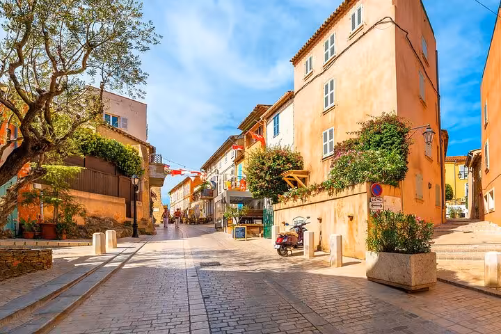 Charming cobblestone street in Saint-Tropez with colorful Mediterranean buildings, flowers, and a parked scooter