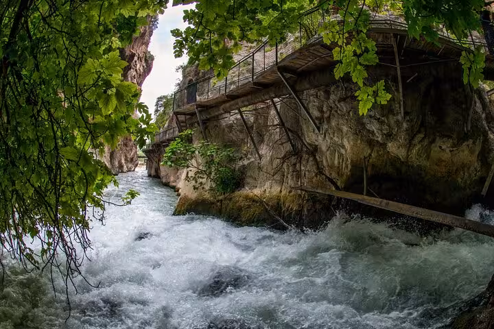 Rushing waters of Saklıkent Canyon with lush greenery and a wooden walkway above the stream in Fethiye.