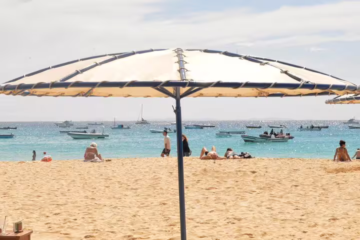 Beachgoers enjoy the sunny shores of Sal Island, lounging under umbrellas with boats dotting the turquoise sea.