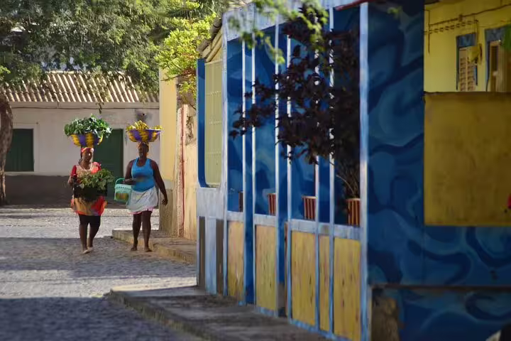 Local women carrying baskets through a colorful street in Santa Maria, Sal Island, private guided island day tour