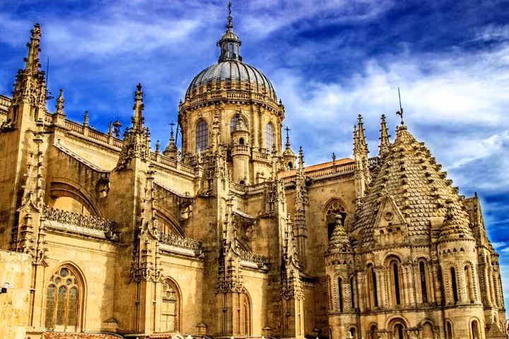 Ornate Gothic and Baroque facade of Salamanca Cathedral with dome and intricate stone carvings under blue sky