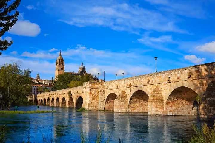View of the historic Roman Bridge and Salamanca Cathedral under a clear blue sky during the Hello Salamanca city walk.