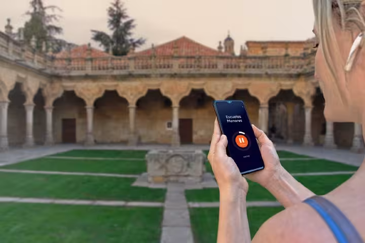 Tourist using audio guide app on smartphone at Escuelas Menores courtyard in Salamanca
