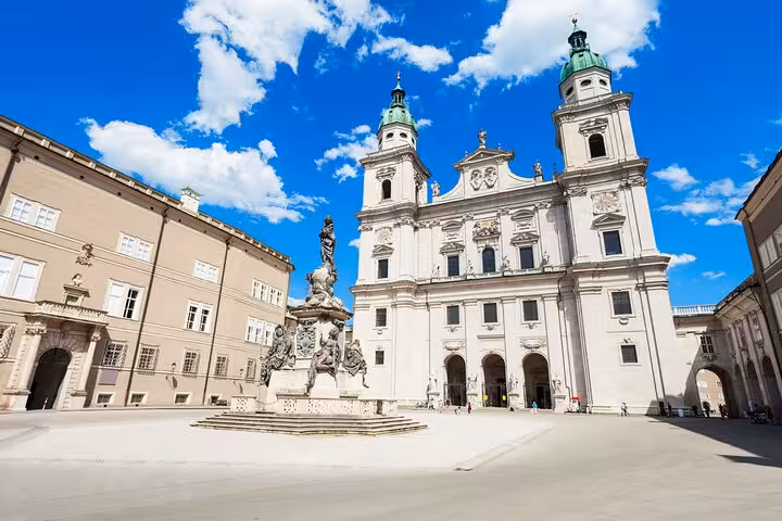 Salzburg Cathedral and Residenzplatz square with baroque column statue under blue sky