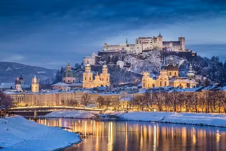 Snowy Salzburg skyline with Hohensalzburg Fortress and river lights on a Christmas markets day trip from Vienna