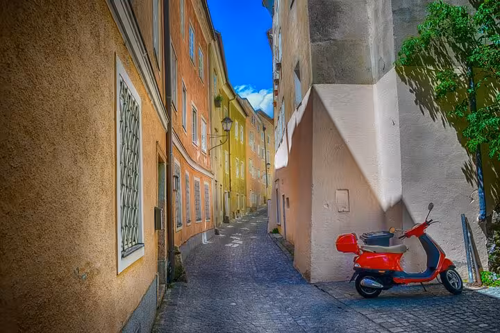 Narrow cobblestone alley in Salzburg Old Town with colorful historic buildings and a red scooter parked