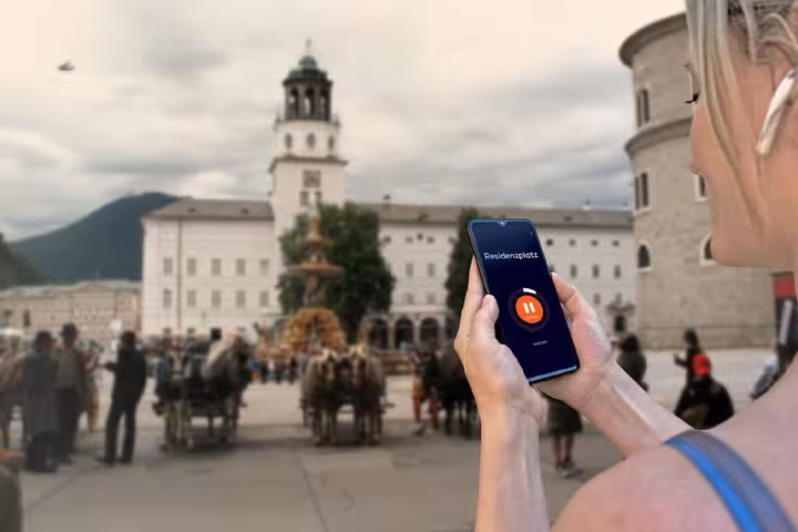 Tourist using GPS audio tour app at Salzburg Residenzplatz with fountain and Glockenspiel tower