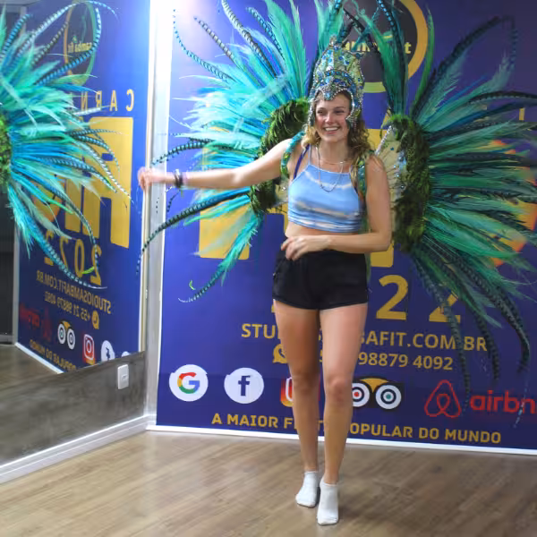A dancer in a colorful carnival costume performs samba during a fun, inclusive class for all levels.