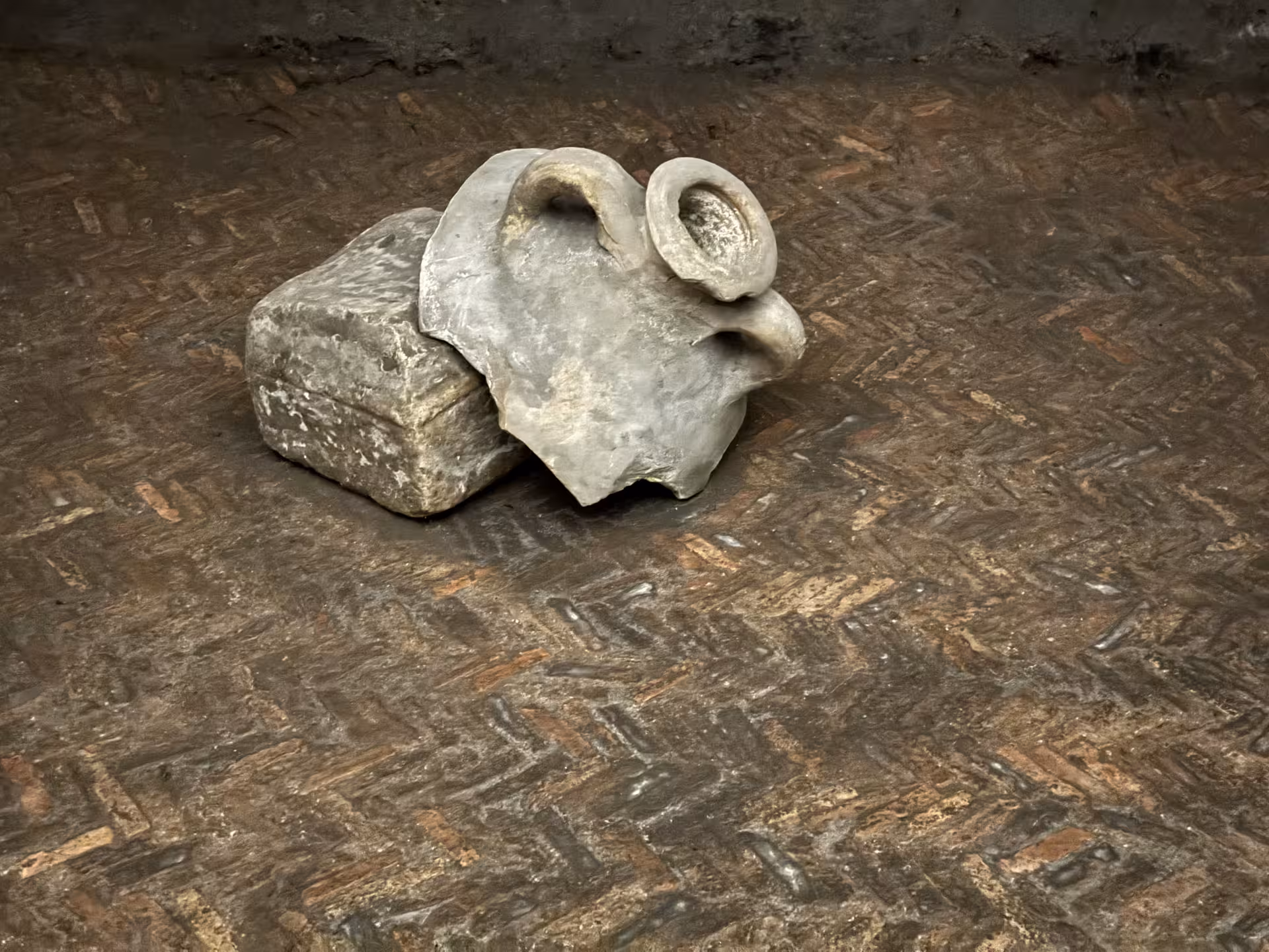Ancient amphora fragments and stone block on worn brick floor in the underground levels of San Clemente Basilica in Rome