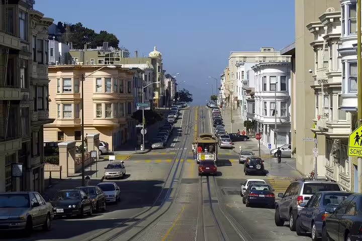 San Francisco cable car on hilly street flanked by Victorian buildings and rail tracks