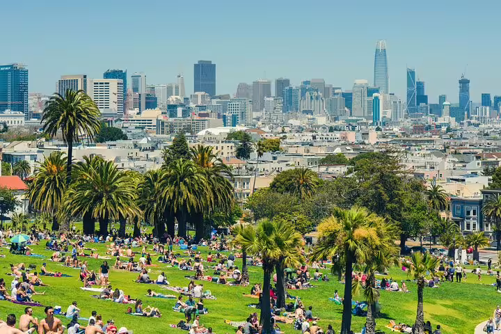 Crowds relaxing on green lawn at Dolores Park with San Francisco skyline and palm trees in background