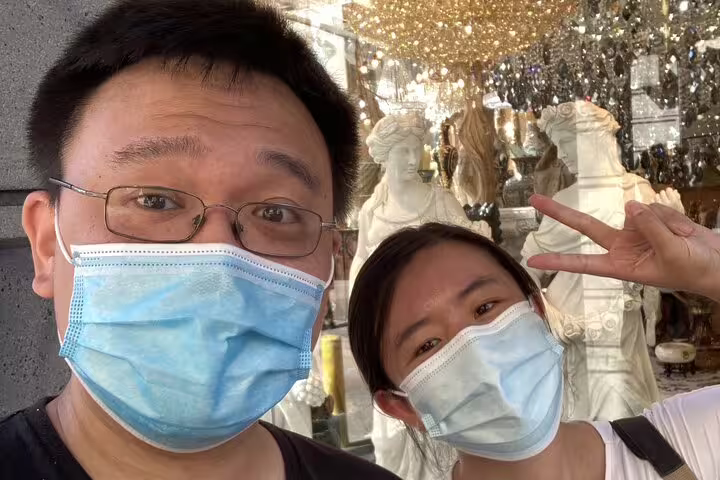 Two visitors wearing masks pose for selfie in front of antique statues during San Francisco walking tour