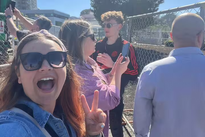 Group of friends smiling and making peace signs outdoors near chain-link fence on San Francisco walking tour