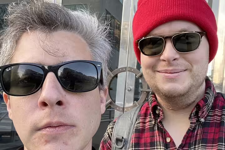 Two men wearing sunglasses taking a selfie outdoors near Hyde Street Pier in San Francisco