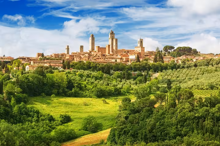 Scenic view of San Gimignano's medieval towers surrounded by lush greenery under a bright blue sky.