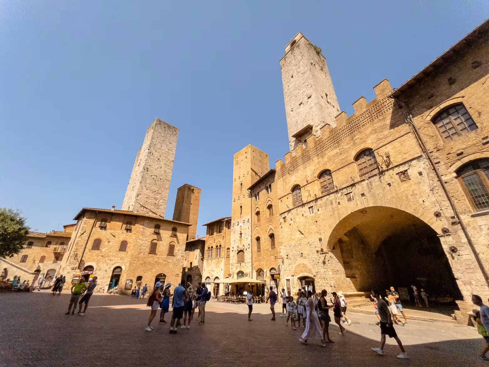 Tourists explore the medieval towers of San Gimignano under a clear blue sky, ideal for a Tuscany day trip.