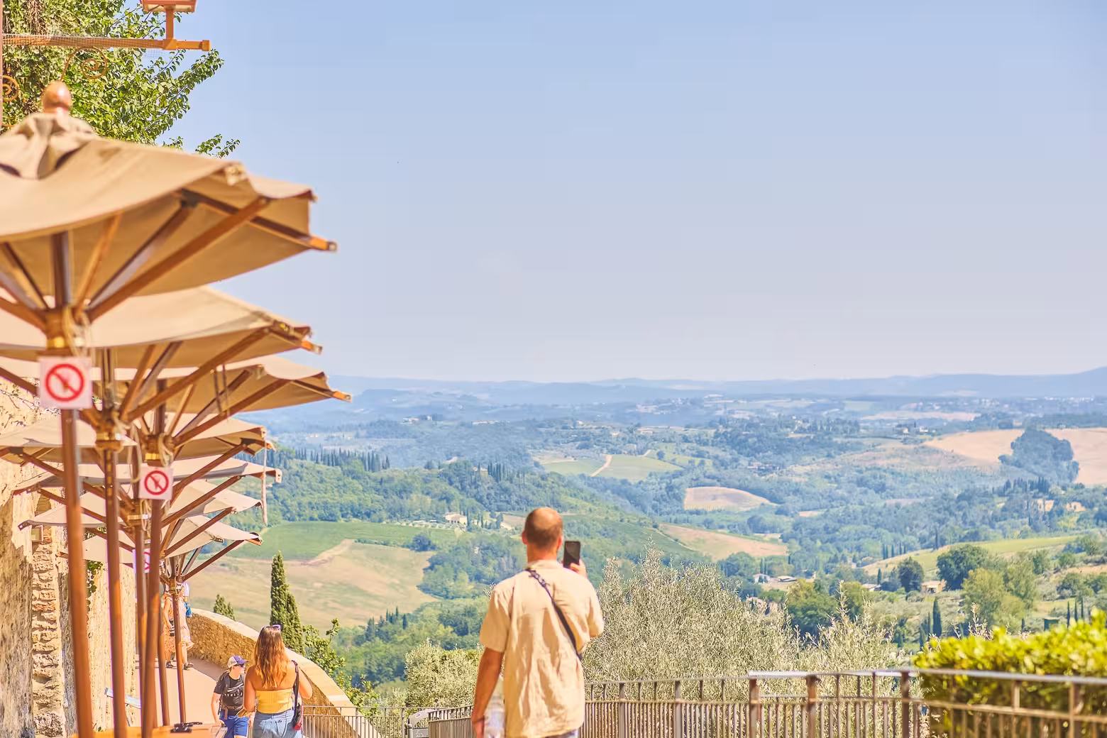 Visitors appreciating the scenic Tuscan landscape from a shaded walkway in San Gimignano.