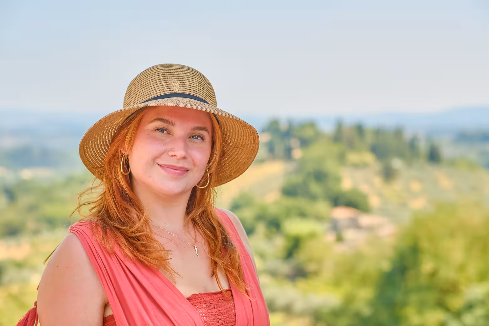 Smiling visitor in a sun hat enjoying the scenic countryside views in San Gimignano, Tuscany.
