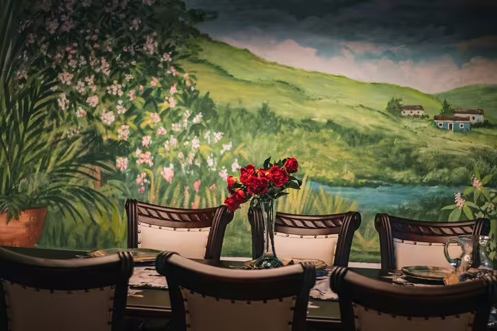 Elegant dining setup with floral centerpiece against a scenic mural backdrop for San Jose By Night tour.