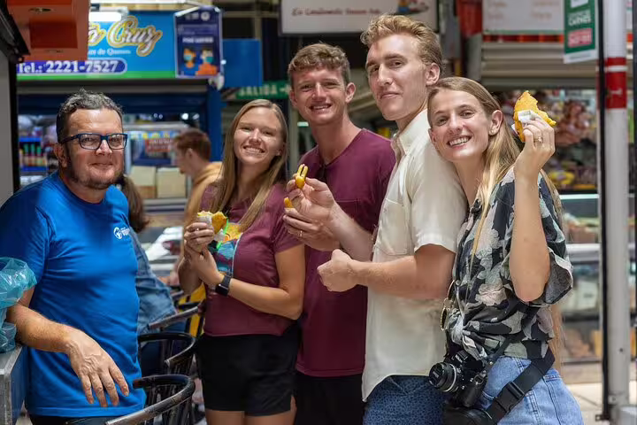 Happy group of tourists sampling fresh market snacks on a San Jose walking food tour.