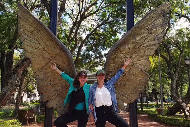 Two women joyfully pose with large angel wings at a scenic spot on the San Jose food tour.