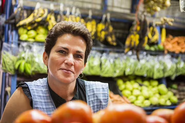 Market vendor in San Jose smiles with fresh produce, highlighting the vibrant food culture on a walking tour.