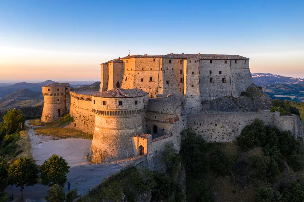 Sunset view of the San Leo fortress perched on a rocky cliff above rolling Montefeltro hills on route 1 guided tour