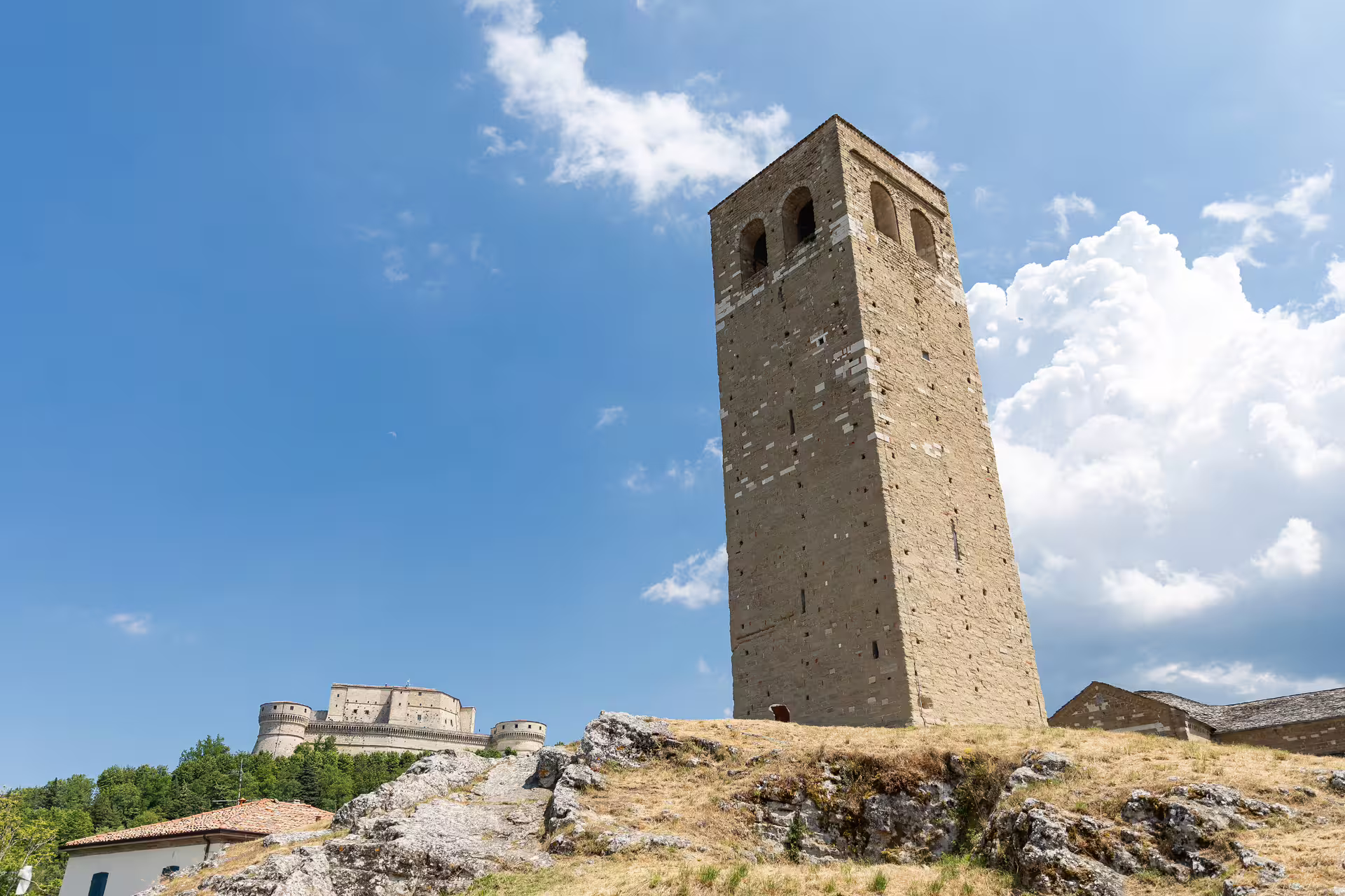 Imposing San Leo Tower rising against a bright blue sky, with fortress visible on a lush green hilltop.