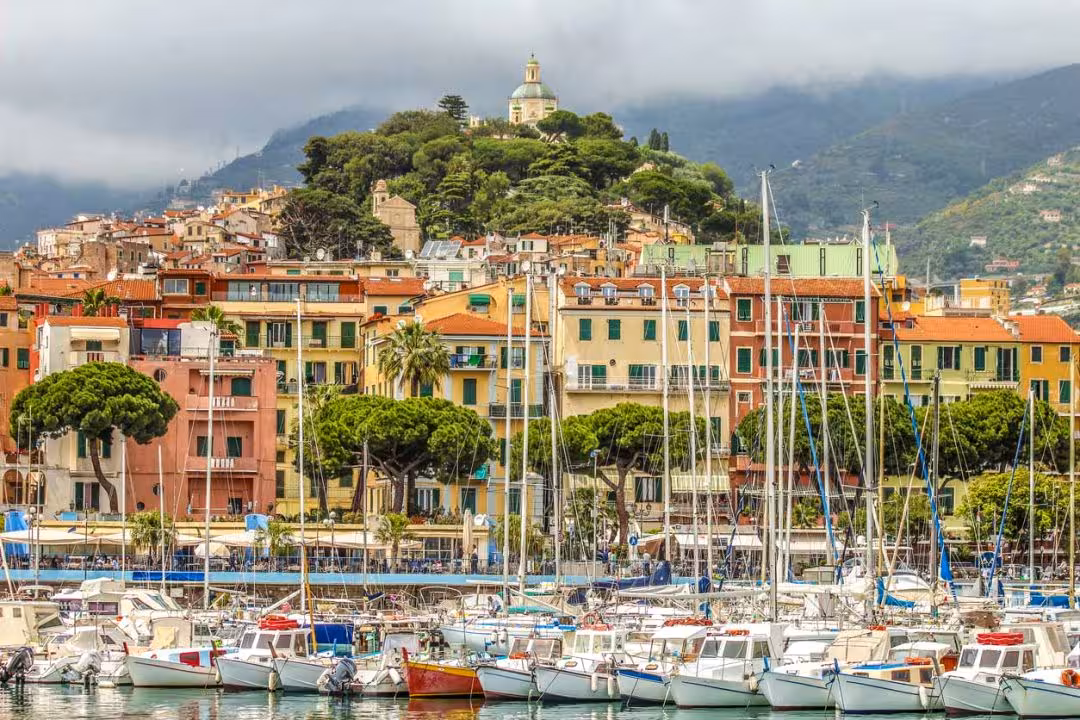 San Remo Italy harbor with colorful buildings, sailboats, and hilltop church dome
