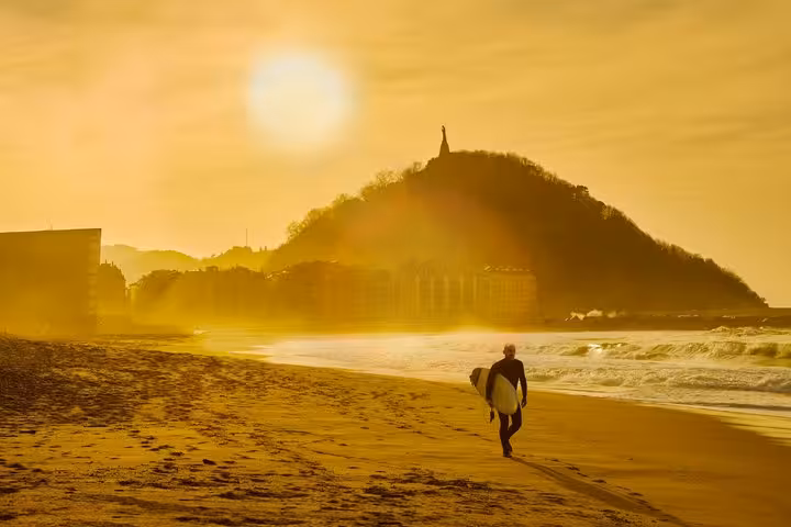 Surfer walking on La Concha Beach at golden sunset with Monte Urgull in San Sebastian, Spain