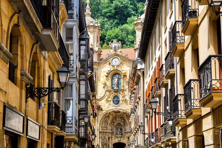 Narrow old town street in San Sebastian with ornate Baroque church facade and clock tower