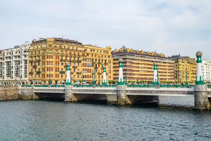 Bridge with green lamp posts over river in San Sebastian Old Town with historic buildings behind
