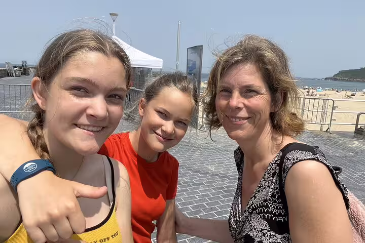 Three women smiling at camera near San Sebastian beach promenade on a sunny day