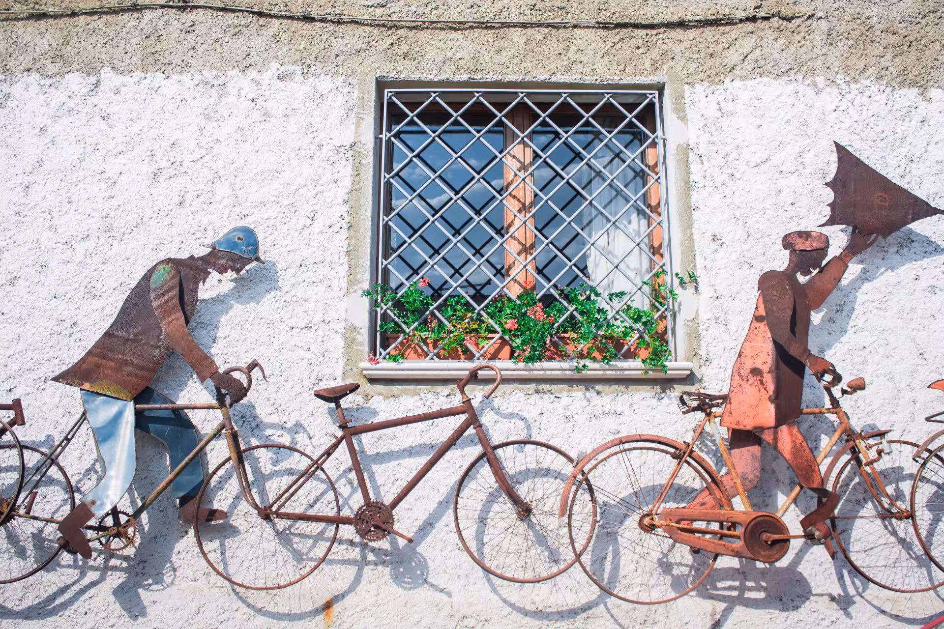Discover vibrant metal sculptures of cyclists on a wall in San Sperate's art-filled village streets.