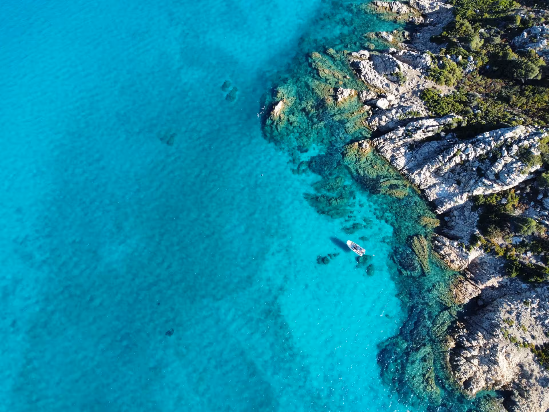 Aerial view of a boat near rocky shores with crystal-clear turquoise waters, perfect for snorkeling in Molara.