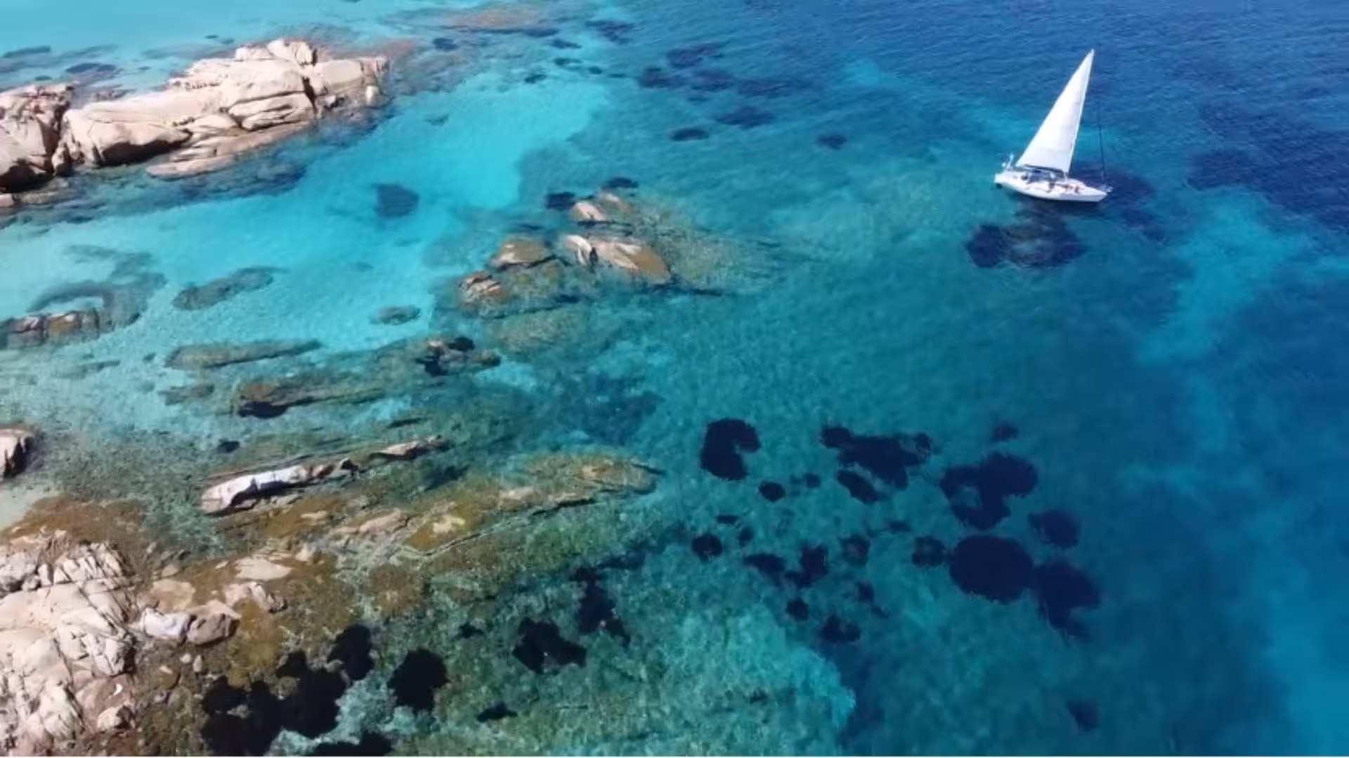 Aerial view of sailboat navigating turquoise waters and rocky coastline near San Teodoro.
