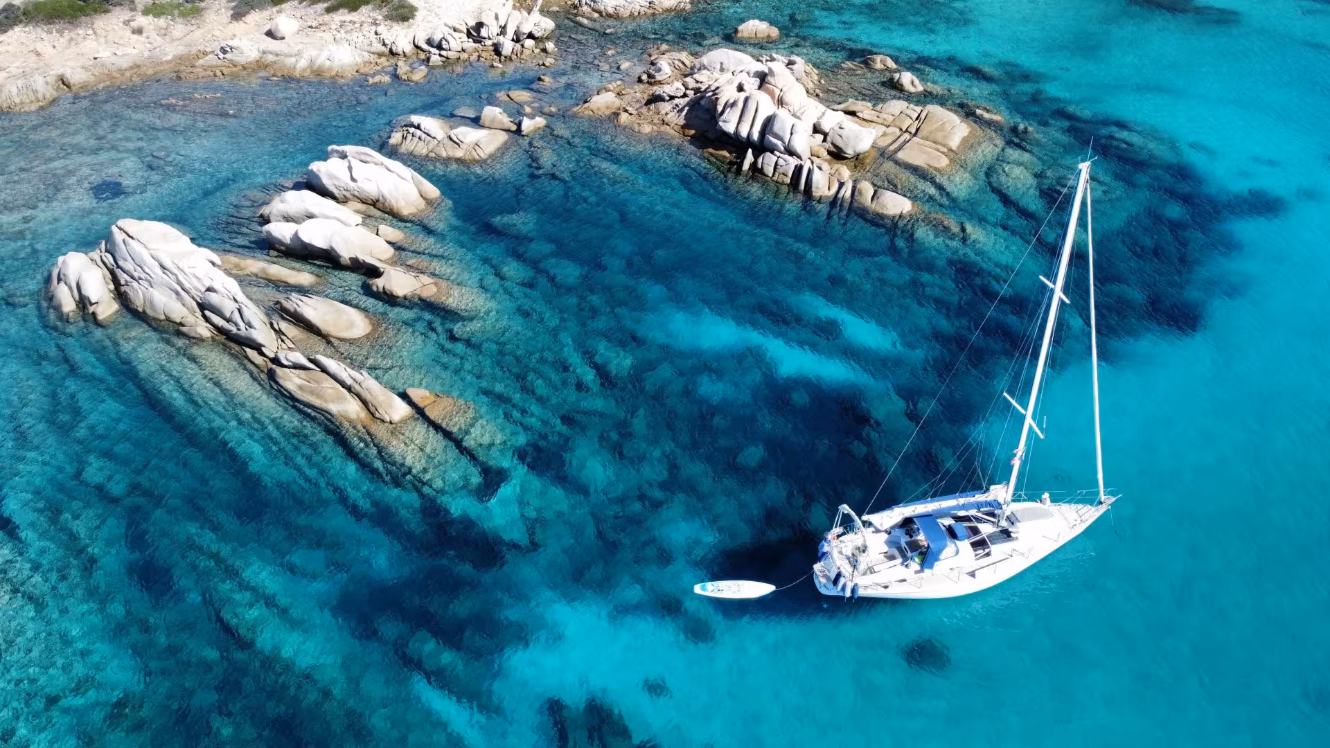 Sailboat anchored in turquoise waters with rocky coastline in the background on the San Teodoro sailing adventure.