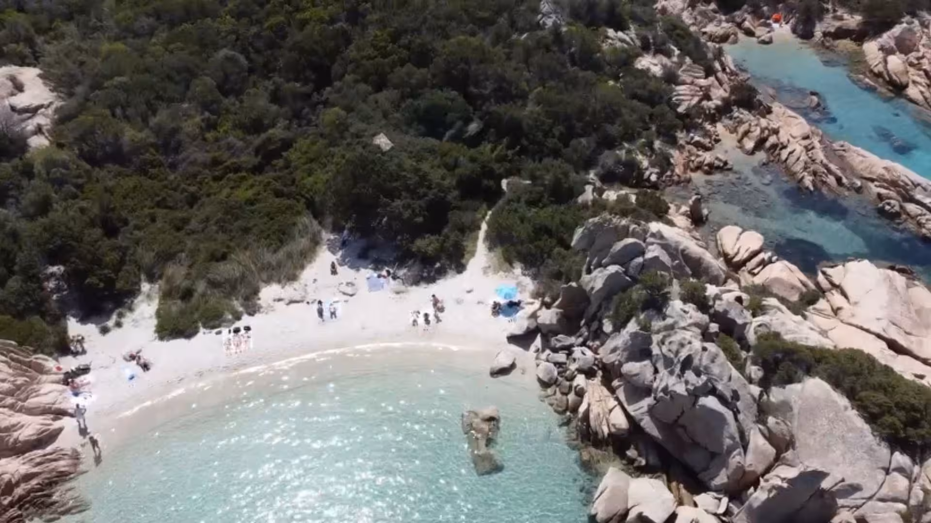 Aerial view of a secluded beach with crystal-clear waters and rocky cliffs on a San Teodoro sailing boat tour.