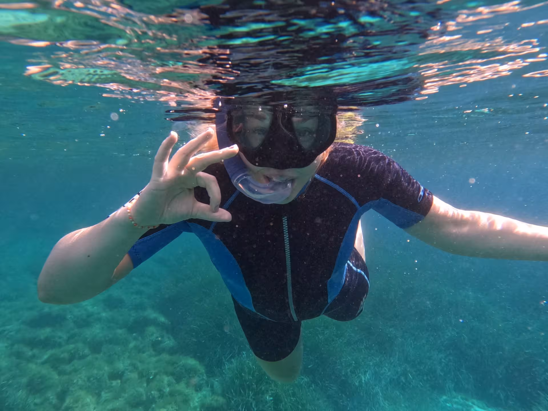 A snorkeler gives an OK sign underwater in the clear waters of Molara, showcasing San Teodoro's marine life.
