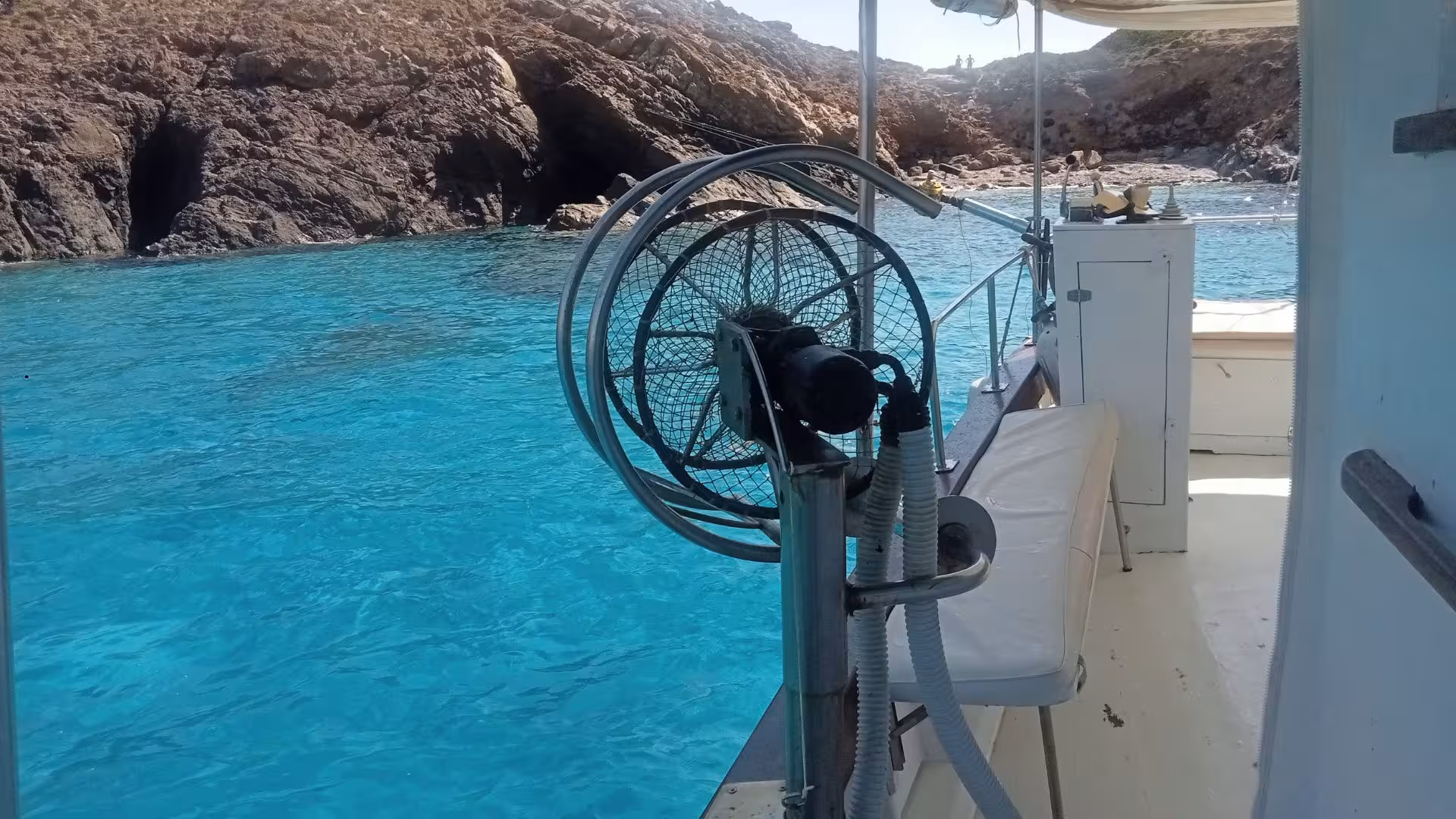 Close-up of a boat deck overlooking the turquoise waters and rocky coastline near Tavolara on a fishing trip from San Teodoro.