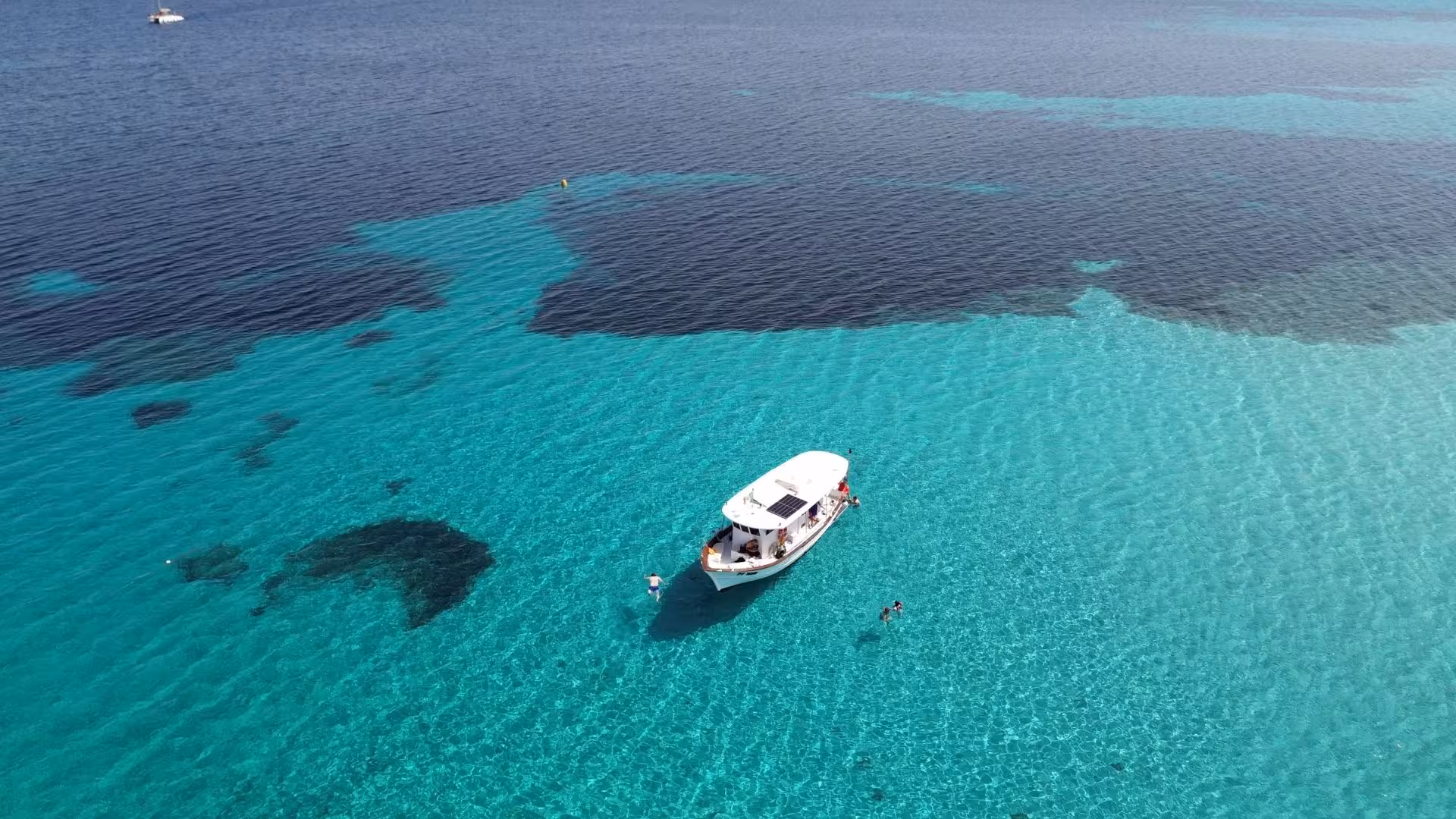 Boat anchored in turquoise waters near Tavolara during a San Teodoro fishing tourism tour.