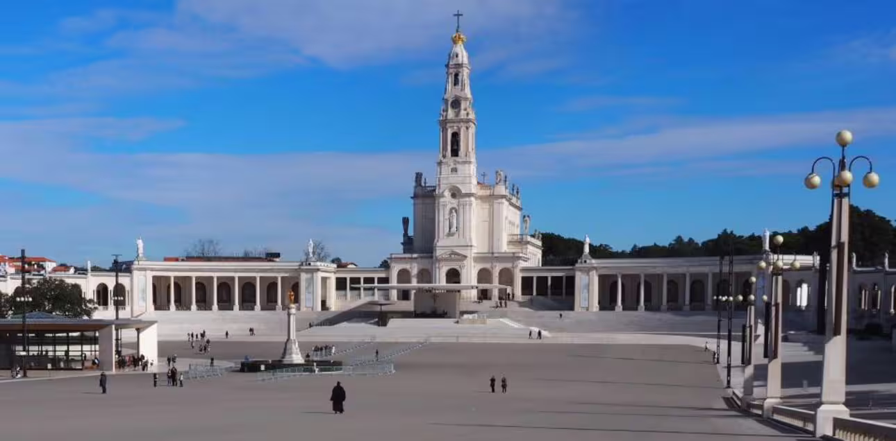 Panoramic view of the Sanctuary of Fátima's impressive exterior and expansive plaza under a clear blue sky.