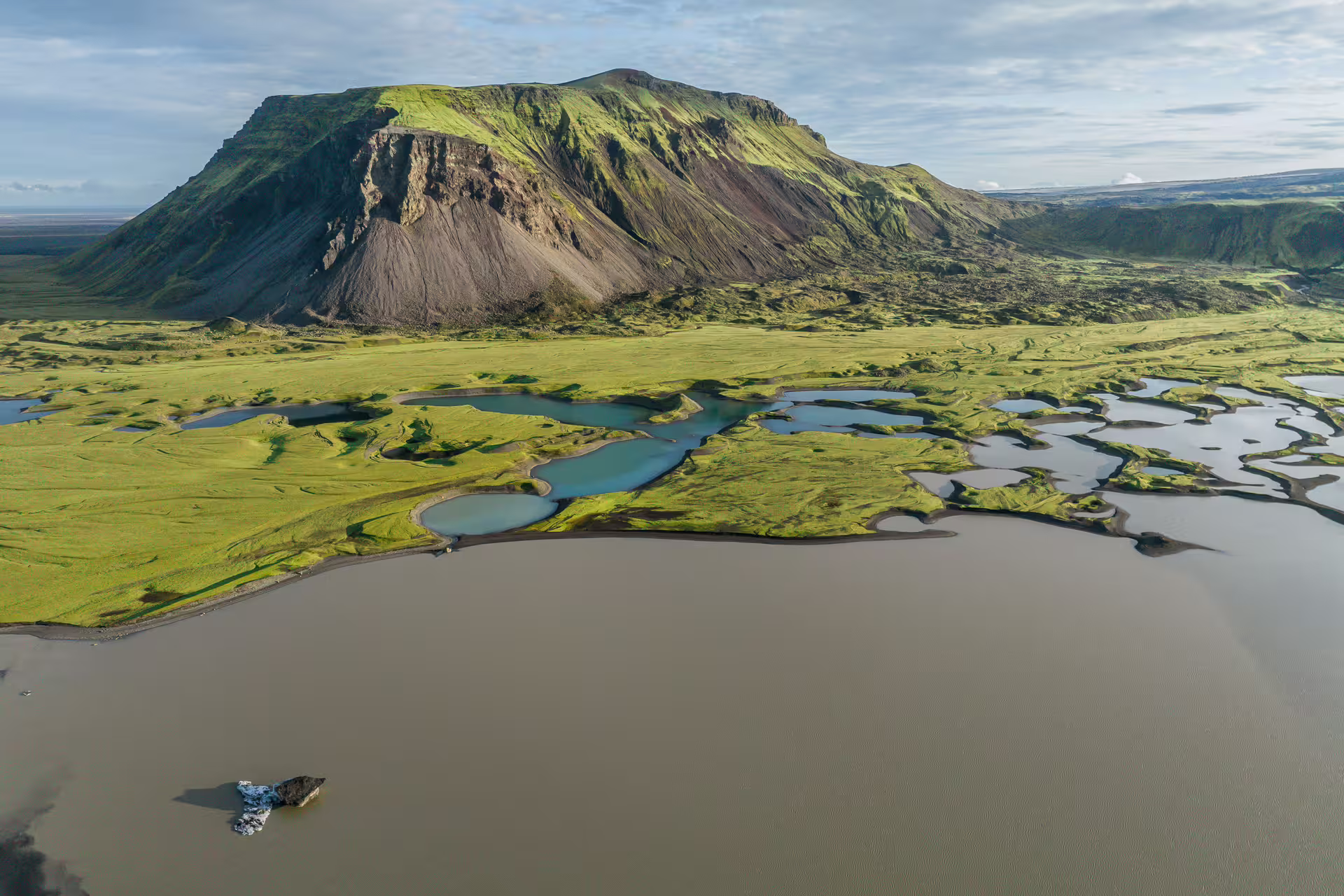 Aerial view of Iceland's dramatic volcanic landscape with lush green moss, glacial rivers, and lakes near Sandfellsjokull Glacier.