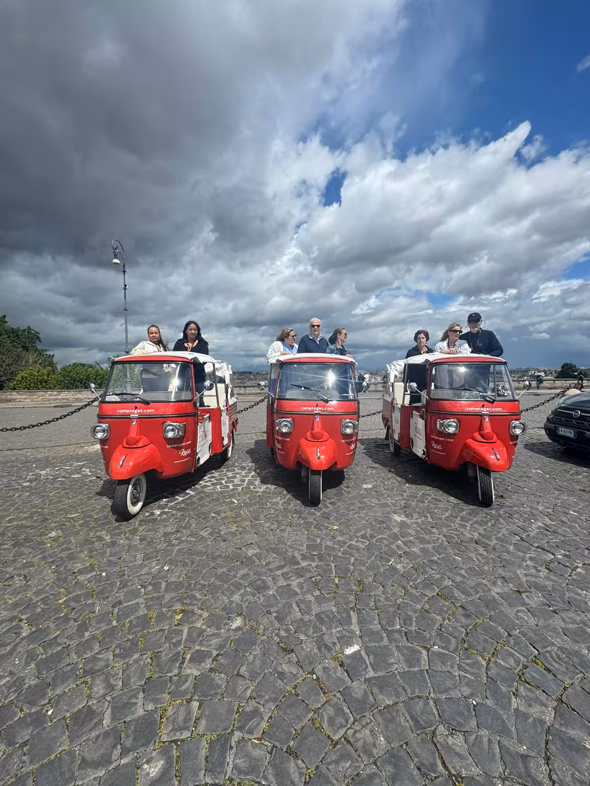 Tourists enjoy a guided ride on vibrant red tuk-tuks near Sant'Angelo Castle under dramatic cloudy skies.