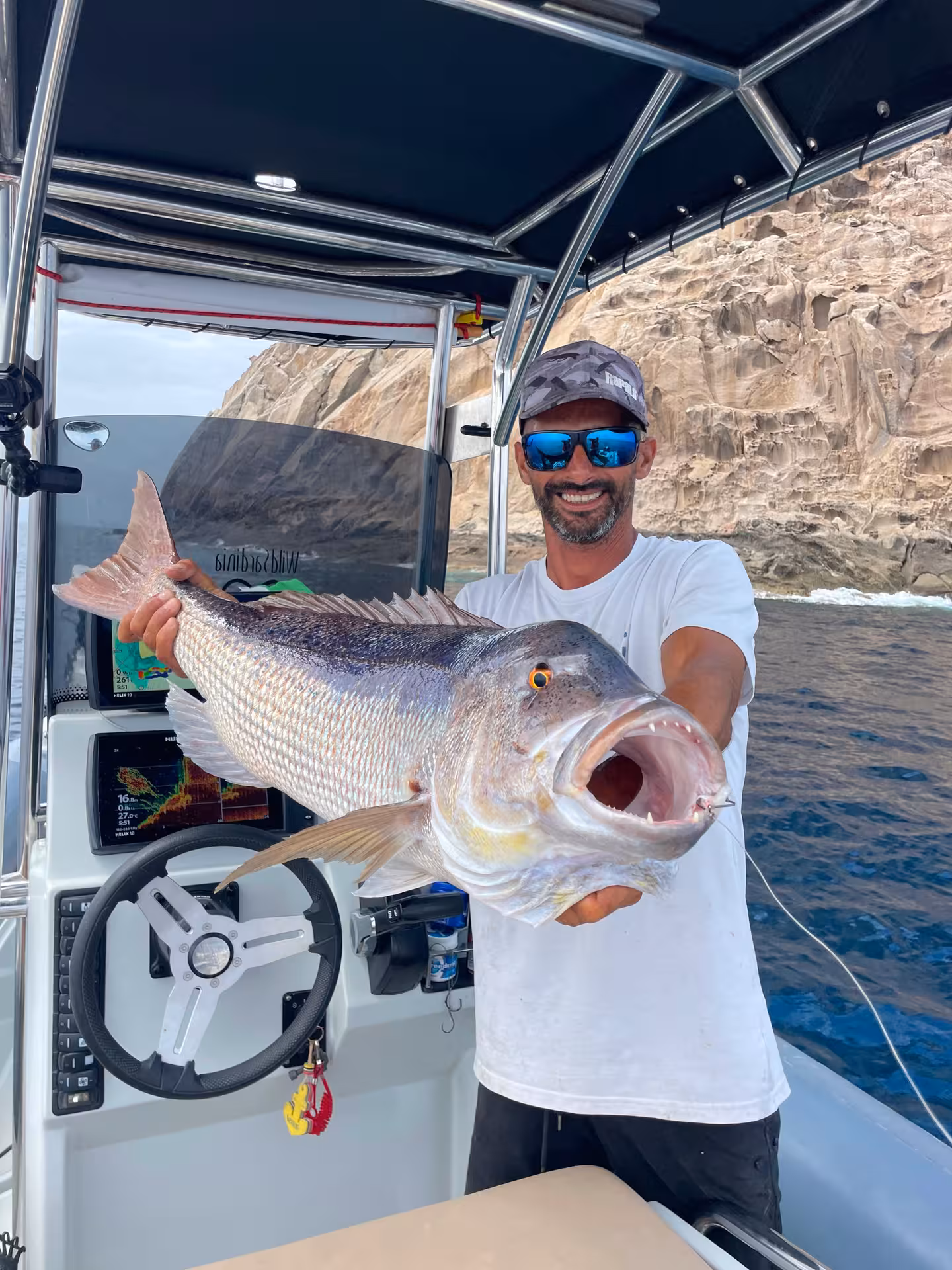 Fisherman proudly displaying a large catch on a Sant'Antioco fishing charter with rocky cliffs in the background.