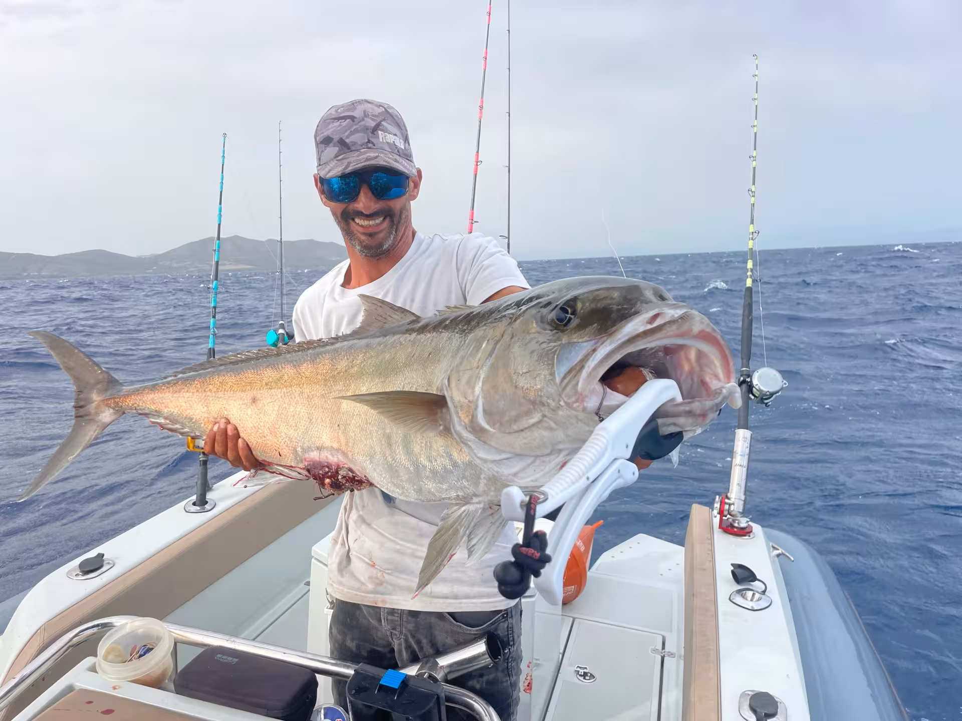 Smiling fisherman displays a giant fish aboard a Sant'Antioco fishing charter in the open sea.
